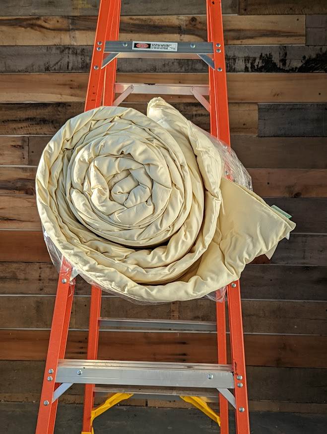 Handmade wool duvet rolled on ladder, eco-friendly bedding from New Zealand wool, temperature-regulating and hypoallergenic.