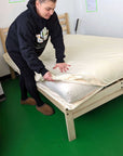 Zippered organic waterproof mattress protector being placed on bed frame