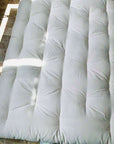 Cotton mattress topper on tiled floor, showcasing plush design and natural material.