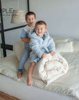 Children sitting on a bed with a cotton mattress topper.