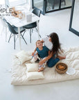 Mother and child sitting on a cotton mattress topper in a bright room with modern decor.