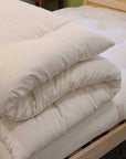 Organic wool mattress topper on a wooden bed frame, handcrafted and made in the USA, offering luxurious comfort and support.