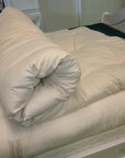 Organic wool mattress topper on bed, rolled for display, showcasing natural plush texture.