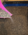 Buckwheat hulls being poured from a pink scoop into a large container.