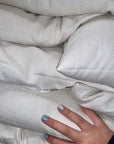 Close-up of a stack of white buckwheat pillows with a hand touching the surface, highlighting the softness and texture.