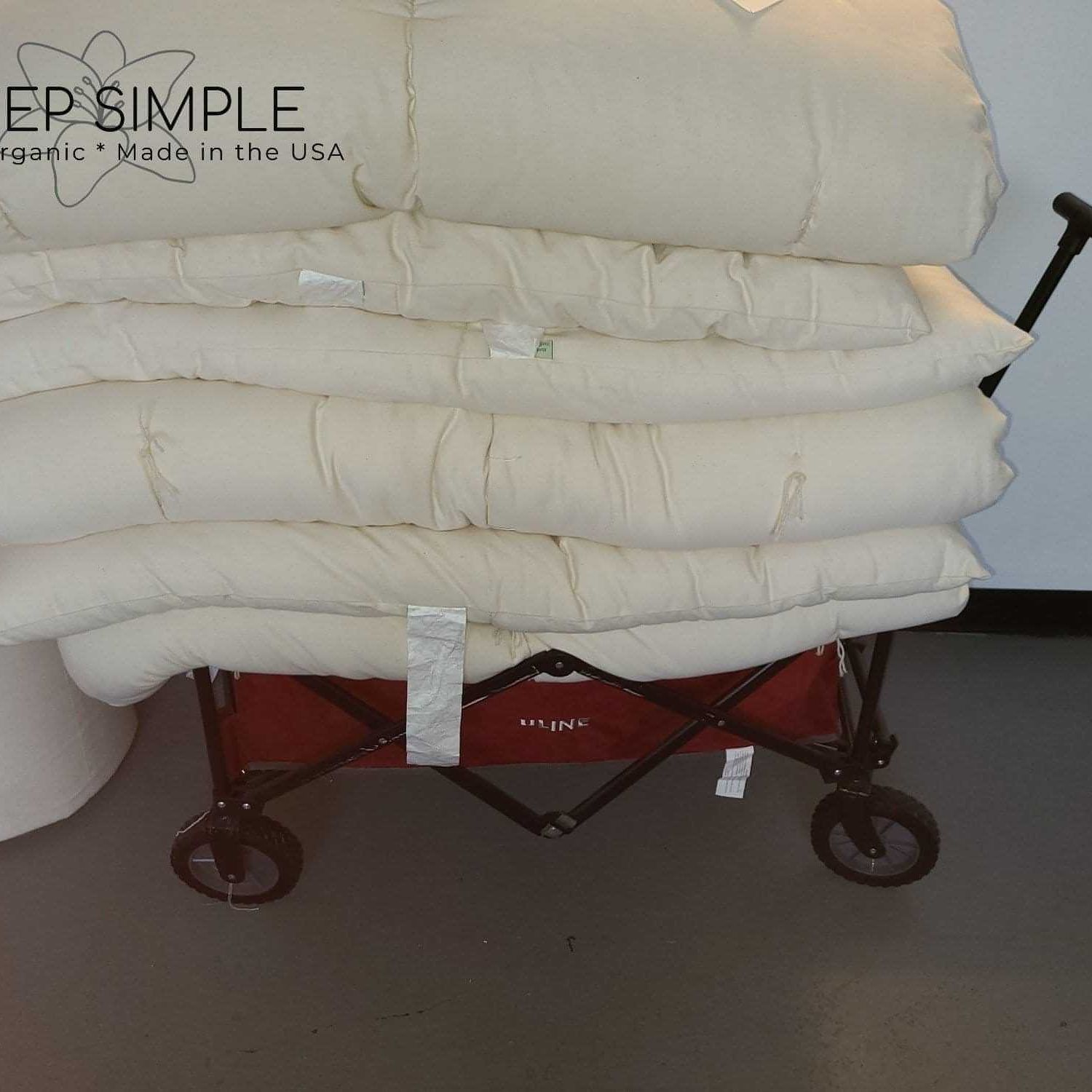 Cotton mattress topper stack on cart, handmade in USA for natural comfort.