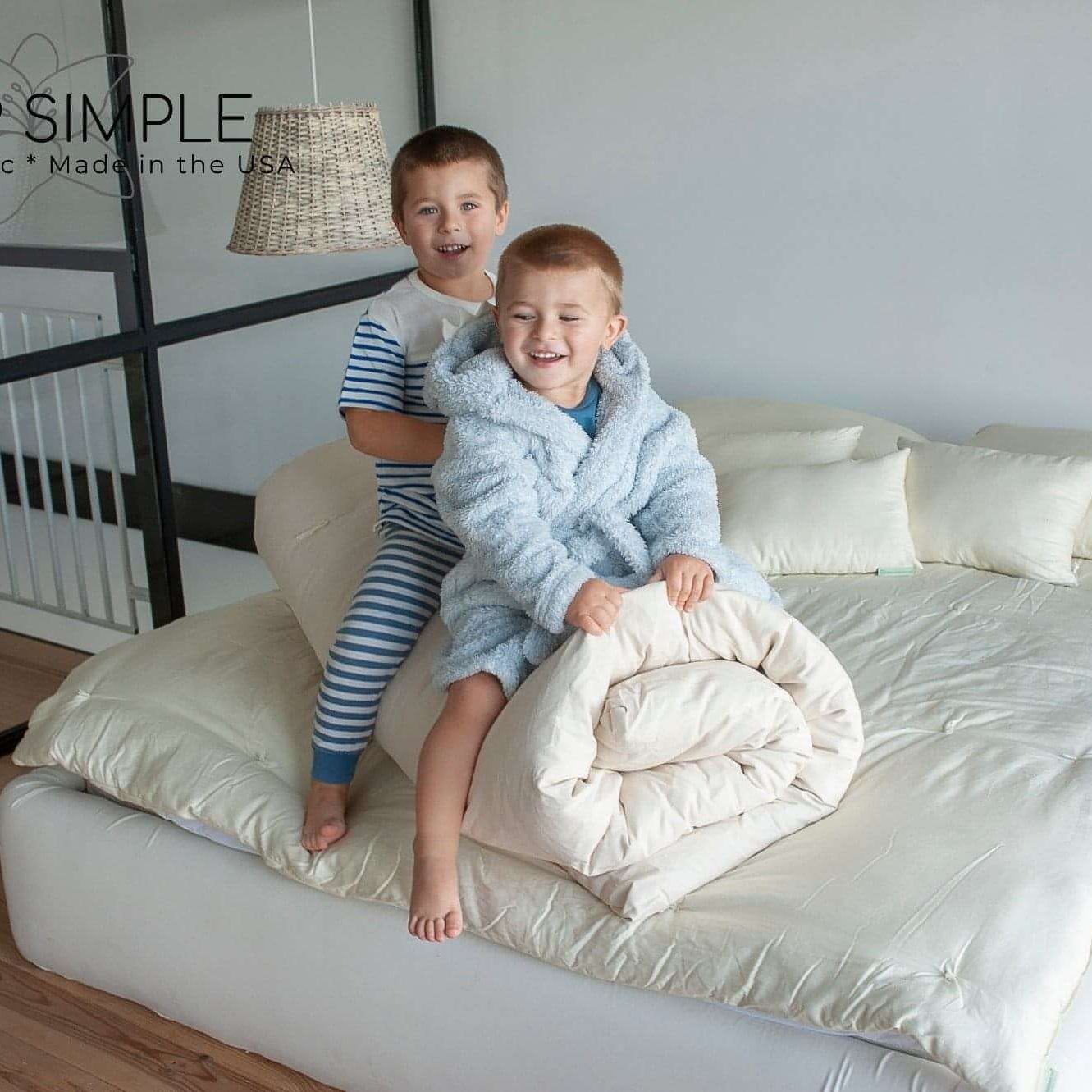 Children sitting on a bed with a cotton mattress topper.