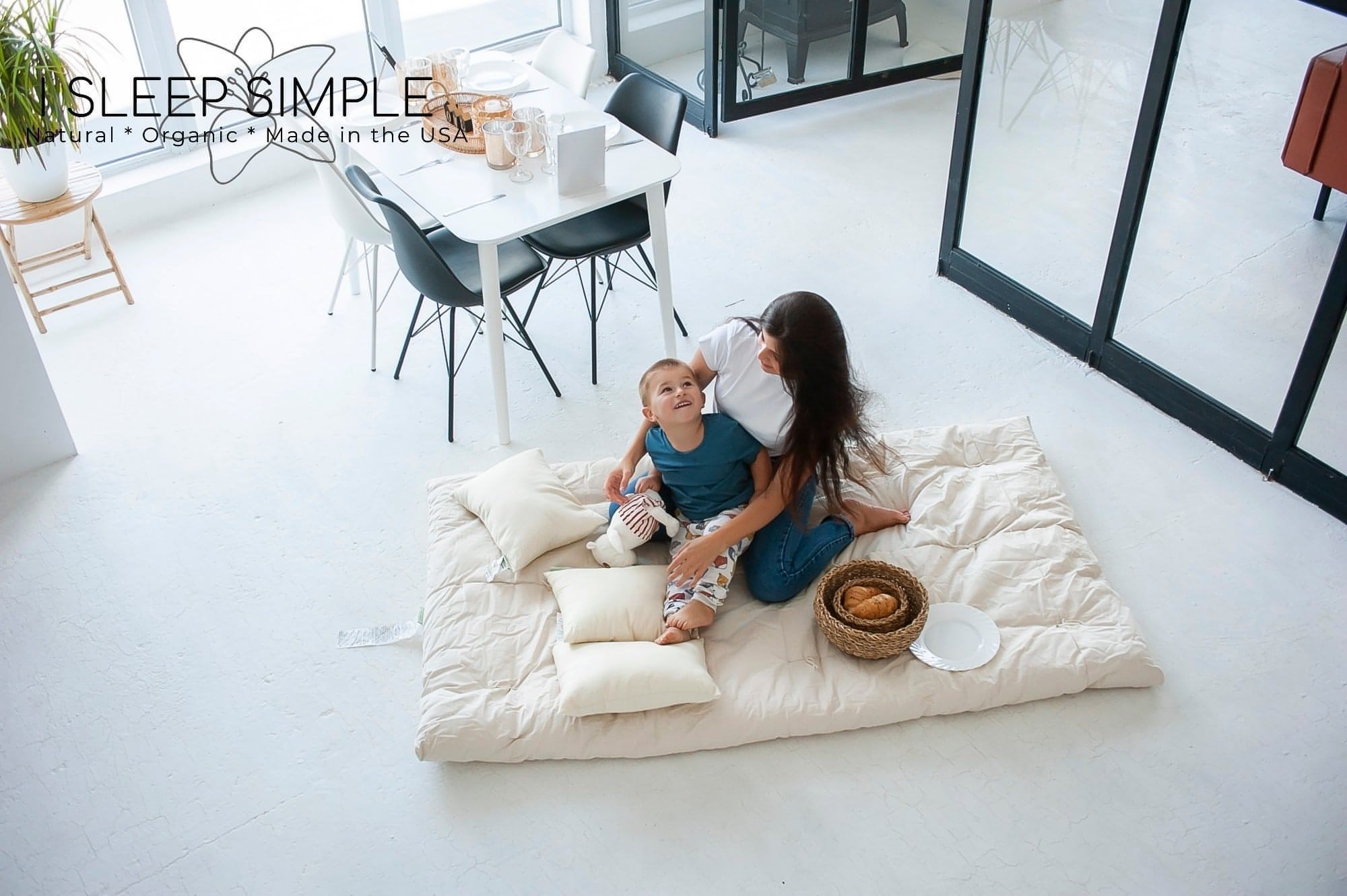 Mother and child sitting on a cotton mattress topper in a bright room with modern decor.