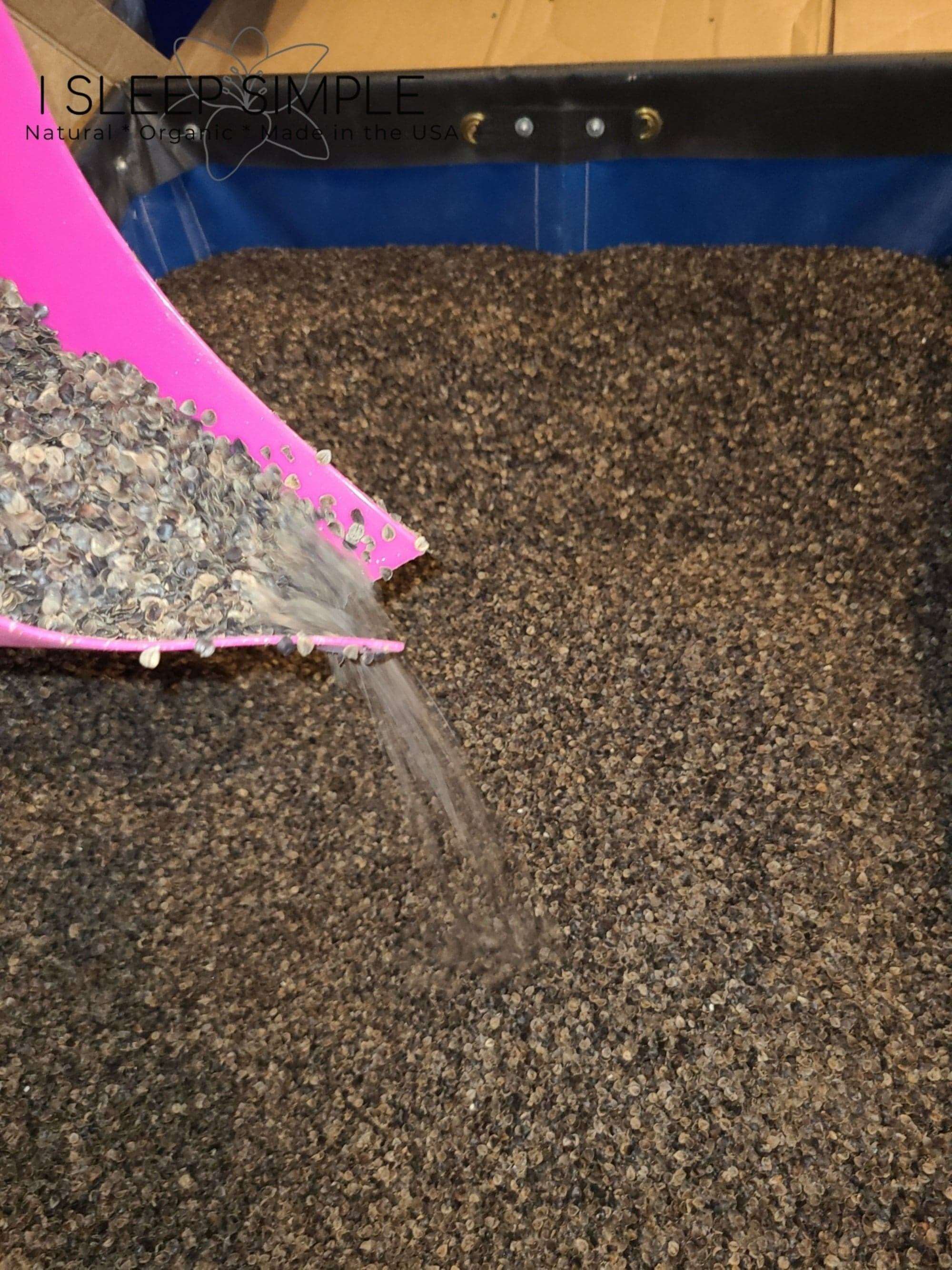 Buckwheat hulls being poured from a pink scoop into a large container.