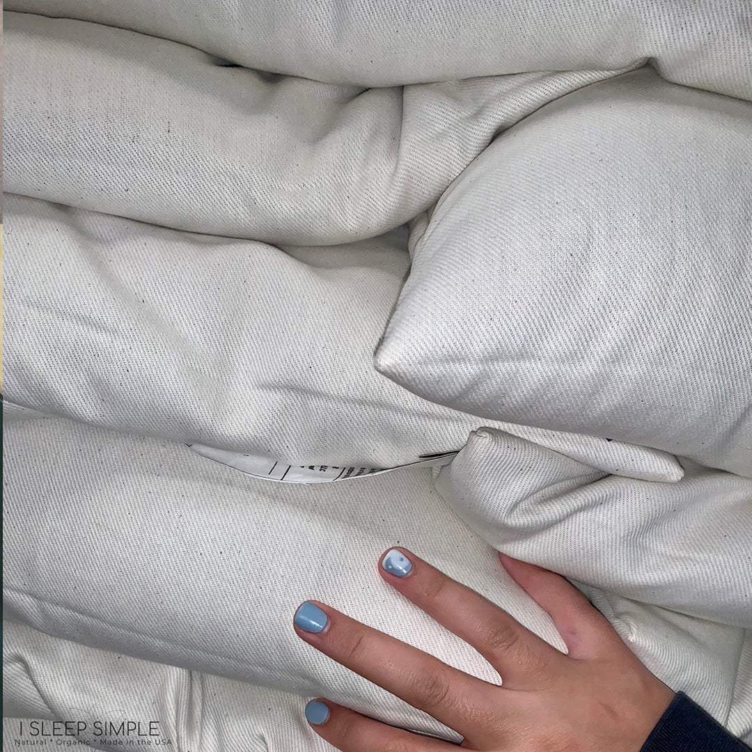 Close-up of a stack of white buckwheat pillows with a hand touching the surface, highlighting the softness and texture.